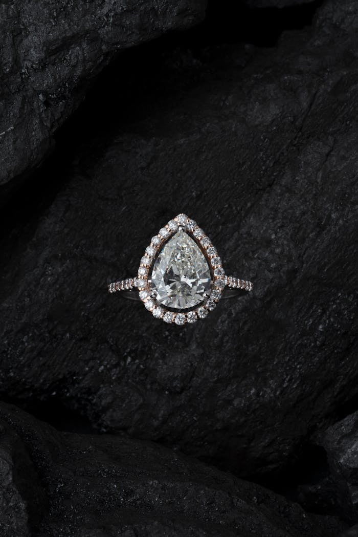 services-04 Stunning teardrop diamond ring surrounded by smaller stones on a textured dark background.