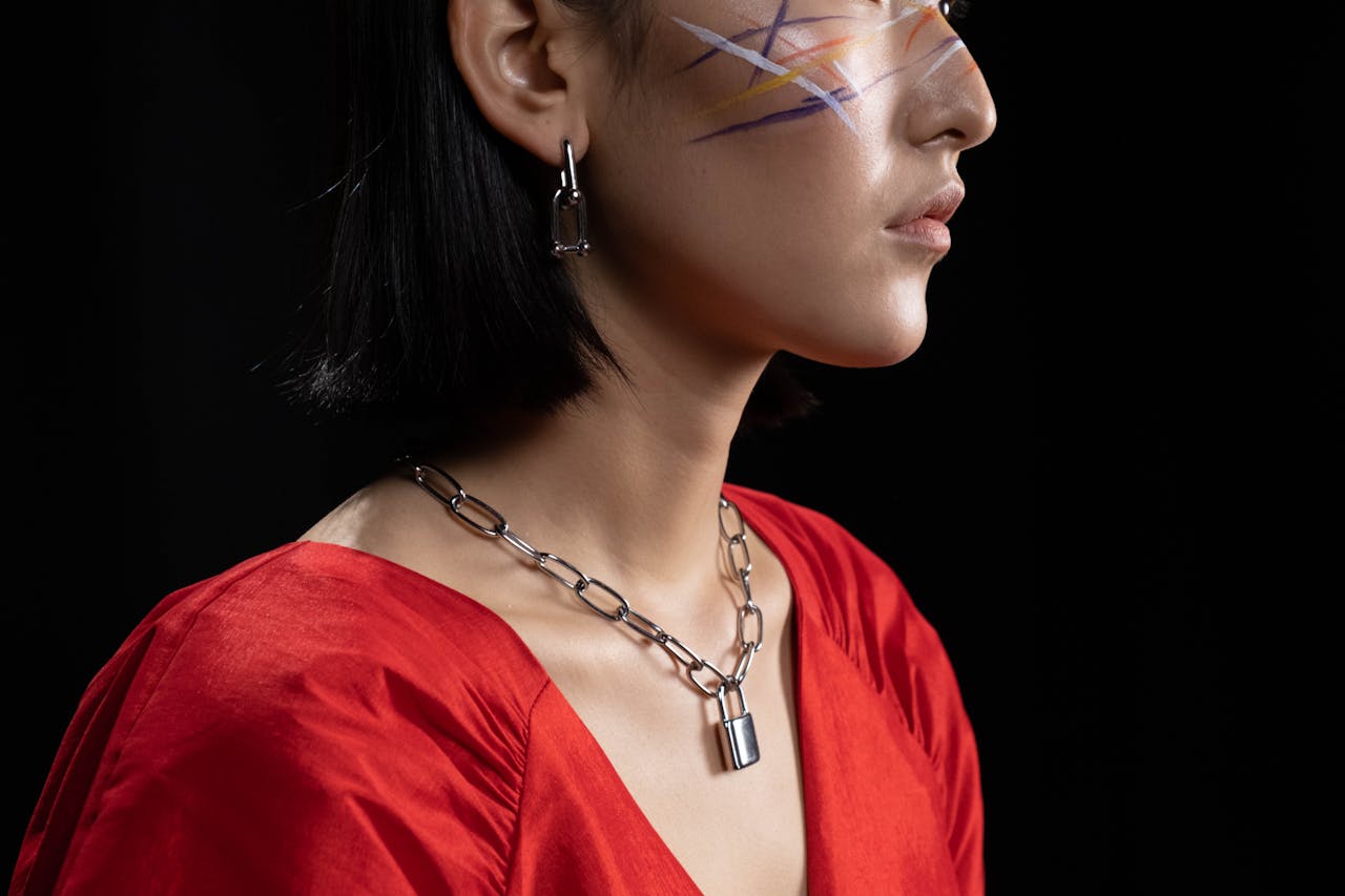 about-us Artistic side profile portrait of a woman with face paint and bold jewelry on a black background.